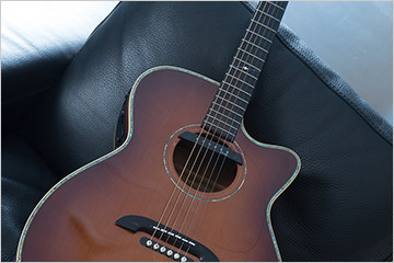 Close-up image of an acoustic guitar sitting on a black leather chair.