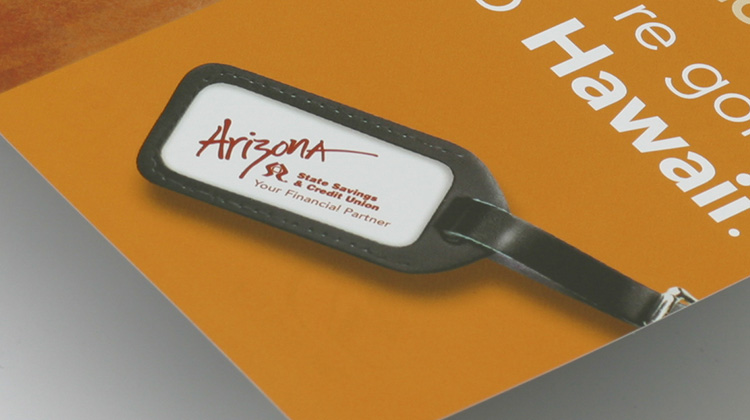 FabCom designed a high-resolution zoomed-in picture for a credit union of a bagtag being displayed on an orange background of a postcard.