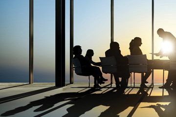 Healthcare IT company advertising campaign image by FabCom of people in a glass office building working at a table with the sun setting in the background.