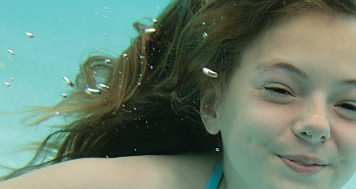High-resolution zoomed-in image showing photographic detail of a print ad FabCom designed. Image shows a young girl swimming under water.