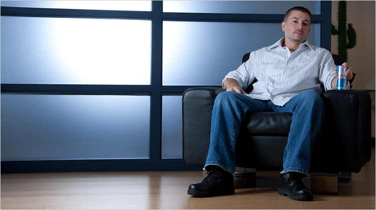 Image of FabCom’s Sr. Producer and Motion Director Lenny sitting in a black leather chair and holding a Red Bull can. Lenny is wearing jeans and a white stripped button-down shirt.