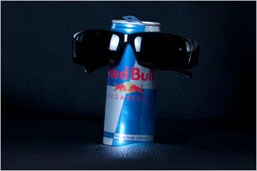 Image of a can of Red Bull seated on a black leather chair and dawning black sunglasses.