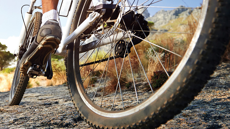 High-resolution zoomed in image showing design detail of a print ad created By FabCom featuring the legs of a man riding a bike on rugged terrain.