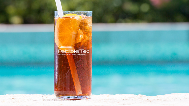 Glass of iced tea with swimming pool finishing company logo on it, with a pool seen in the background.