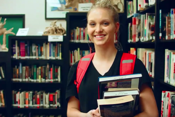 Student smiling in library with books.