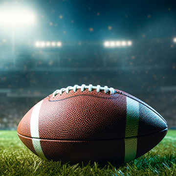 Close-up of a football resting on the grass at the center of a stadium.