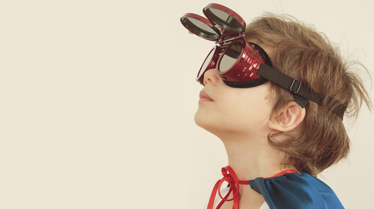High-resolution image of young boy wearing a hero cape and Back-to-the-future style goggles that emulate a future technology university student.